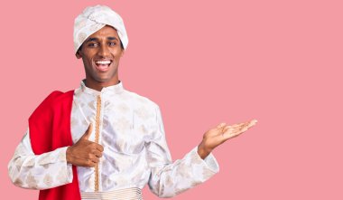 Afrikalı yakışıklı adam geleneksel Sherwani sari elbisesi giyiyor avuç içi gösteriyor ve baş parmaklarıyla iyi bir hareket yapıyor, mutlu ve neşeli gülümsüyor. 