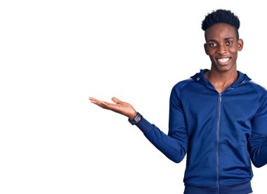 Afro-Amerikalı genç bir adam spor kıyafetleri giyiyor. Gülümsüyor, iki elini de açık tutuyor. Karşılaştırma, reklam karşılaştırma ve denge yapıyor. 