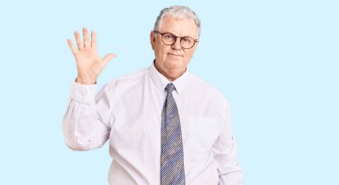 İş kıyafetleri giymiş yaşlı, gri saçlı bir adam beş numarayı gösterip işaret ederken kendinden emin ve mutlu bir şekilde gülümsüyor.. 