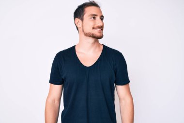 Gündelik giysiler giymiş genç yakışıklı bir adam yüzünde gülümsemeyle yan yana bakıyor, doğal bir ifade. Kendinden emin gülen. 