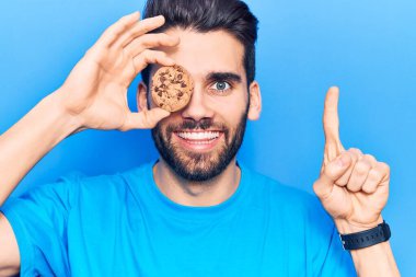 Sakallı, elinde çikolatalı kurabiye olan genç yakışıklı bir adam bir fikirle gülümsüyor ya da mutlu bir yüzle işaret ediyor. 