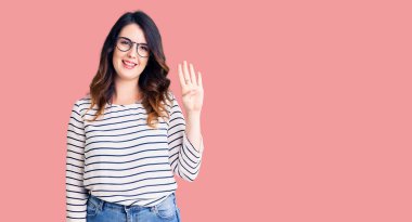 Güzel, genç, esmer bir kadın günlük kıyafetler ve gözlük takıyor. Dört numarayı gösteriyor ve işaret ediyor. Kendinden emin ve mutlu bir şekilde gülümsüyor.. 