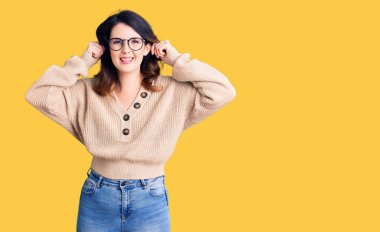 Güzel, genç, esmer bir kadın. Günlük kıyafetler ve gözlük takıyor. Gülümsüyor, kulakları parmaklarıyla çekiyor. deneme sorunu 