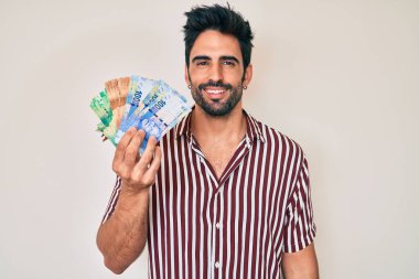 Sakallı yakışıklı İspanyol adam Güney Afrika rand banknotları tutuyor. Pozitif ve mutlu görünüyor. Kendine güvenen bir gülümsemeyle dişlerini gösteriyor. 