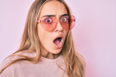 Kalp şeklinde güneş gözlüğü takan genç, güzel sarışın kadın şaşkınlık ve şaşkınlık dolu bir ifade, korku ve heyecan dolu bir yüz ifadesiyle dehşete düşmüş ve şok olmuştu.. 