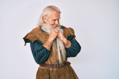 Gri saçlı, uzun sakallı, Viking kostümü giyen yaşlı bir adam. Gergin ve heyecanlı bir şekilde çenesinin kenarına bakıyor. 