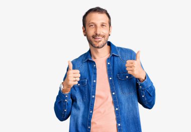 Gündelik kıyafet giyen yakışıklı bir adam. Başarı işareti yapıyor. Elleriyle olumlu jest yapıyor. Neşeli ifade ve kazanan jest. 