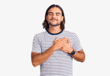 Sıradan kıyafetler giyen, elleri göğsünde, gözleri kapalı gülümseyen ve yüzünde minnet ifadesi olan genç yakışıklı bir adam. sağlık kavramı. 