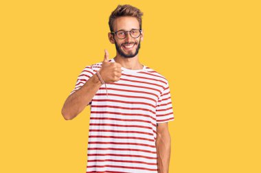 Sakallı, sıradan kıyafetler ve gözlük takan yakışıklı sarışın el hareketleriyle mutlu mesut selam veriyor. Kameraya bakıp başarıyı gösteren ifade. 