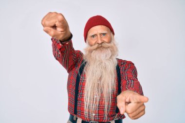 Gri saçlı ve uzun sakallı yaşlı bir adam. Hipster görünümlü, yün şapkalı, parmaklarıyla kamerayı gösteren, neşeli ve pozitif gülümseyen biri. 