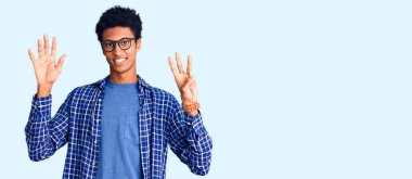 Genç Afro-Amerikan adam günlük kıyafetler ve gözlük takıyor. Sekiz numaralı parmaklarıyla gösteriyor ve işaret ediyor. Kendinden emin ve mutlu gülümsüyor.. 