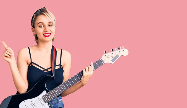 Młoda Piękna Blondynka Gra Gitarze Elektrycznej Uśmiechnięta Szczęśliwy Wskazując Ręką — Zdjęcie stockowe