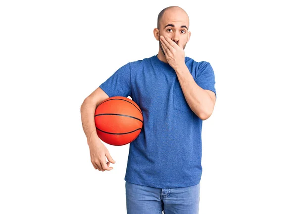 若いハンサムな男は手で口をカバーバスケットボールボールを保持し ショックを受け 間違いを恐れている 驚きの表情 — ストック写真