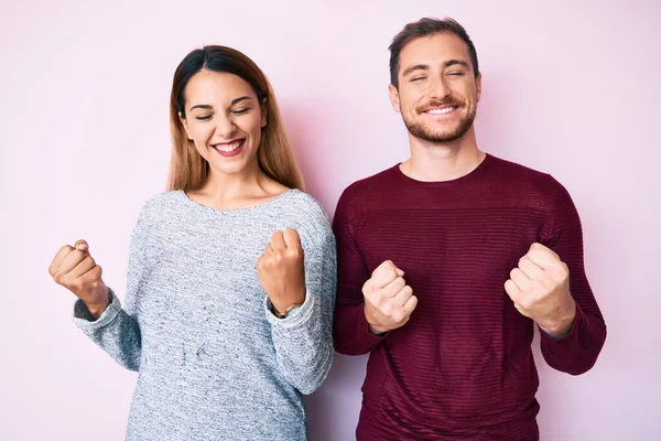Başarılı olmak için heyecanlı giysiler giyen güzel bir çift kolları havada ve gözleri kapalı zaferi kutlarken gülümsüyor. Kazanan konsept. 