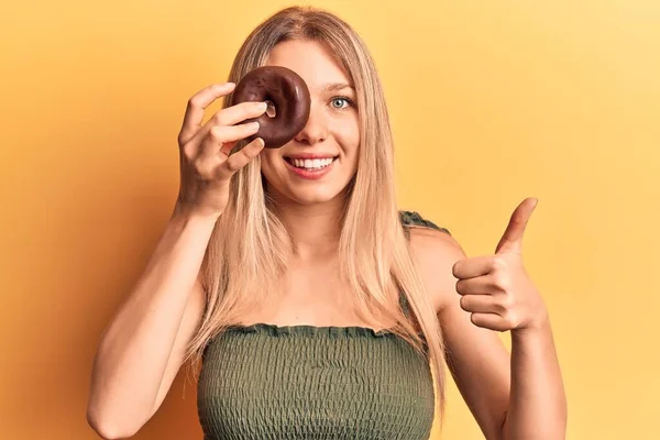 Genç Sarışın Kadın Elinde Donut Tutarken Mutlu Pozitif Gülümsüyor Başparmağıyla — Stok fotoğraf