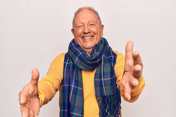 Senior handsome grey-haired man wearing casual scarf over isolated white background looking at the camera smiling with open arms for hug. Cheerful expression embracing happiness.