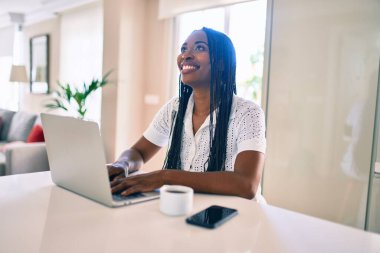 Genç Afro-Amerikan kadın mutlu bir şekilde gülümsüyor. Evde dizüstü bilgisayar kullanıyor.