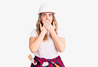 Güvenlik kaskı takan genç beyaz kadın yanlışlıkla ağızlarını kapatarak şok geçirdi. gizli kavram. 