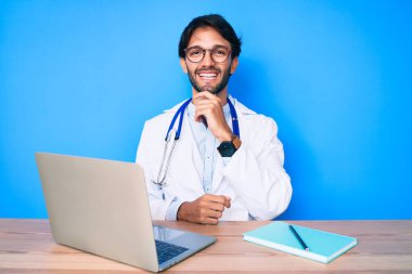 Klinikte çalışan yakışıklı, doktor üniforması giyen, gülümseyen kolları çapraz ve çenesi açık kameraya bakan yakışıklı bir adam. Olumlu düşünmek. 