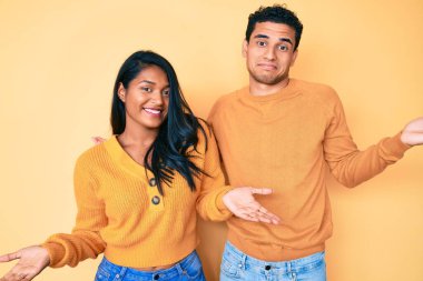 Güzel Latin genç çift, günlük kıyafetlerini giyip gülümseyerek avuçlarını açıyor, sunuyor ve reklam karşılaştırması yapıyor ve dengeyi sağlıyor. 
