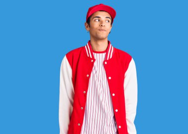 Beyzbol forması giyen genç Afrikalı Amerikalı adam gülümsüyor, yan tarafa bakıyor ve düşünüyor.. 