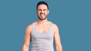 Mayolu ve kolsuz tişörtlü genç yakışıklı adam komik bir ifadeyle dilini dışarı çıkarıyor. duygu kavramı. 