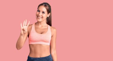 Genç ve güzel İspanyol kadın spor giysisi giyiyor ve dört numarayı gösterip işaret ederken kendine güvenen ve mutlu bir şekilde gülümsüyor.. 