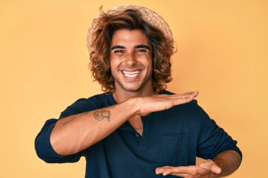 Yazlık şapkalı genç İspanyol adam. Elleriyle işaret ediyor. Büyük ve büyük boy işareti, ölçü işareti. Kameraya bakıp gülümsüyor. ölçüm kavramı. 
