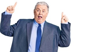 İş ceketi giyen yaşlı gri saçlı adam şaşırmış, şaşırmış ve parmaklarıyla işaret ediyor ve kollarını kaldırıyordu.. 