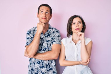 Güzel bir çift, elleri çenelerinde gündelik giysiler giyip soru sormayı düşünüyorlar. Düşünceli bir ifade. Gülümseyen ve düşünceli bir yüz. şüphe kavramı. 