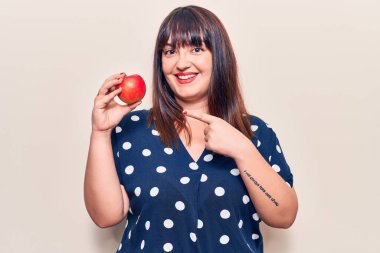 Elinde kırmızı elma tutan genç ve iri bir kadın mutlu mesut elini ve parmağını gösteriyor. 