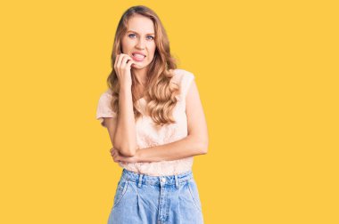 Sarı saçlı, rahat kıyafetler giyen, gergin ve gergin görünen, elleri ağızdan tırnak yiyen güzel beyaz bir kadın. anksiyete. 