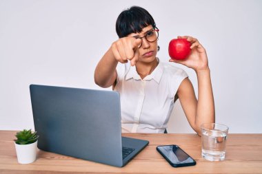 Ofiste çalışan güzel bir esmer kadın sağlıklı elmalar yiyor kamerayı işaret ediyor ve kendine güveni tam bir jest yapıyorsun. 