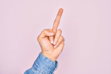 Hand of caucasian young man showing fingers over isolated pink background showing provocative and rude gesture doing fuck you symbol with middle finger