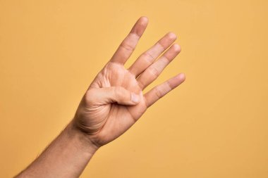 İzole edilmiş sarı arka planda parmaklarını gösteren beyaz bir gencin eli dört parmağı gösteriyor.