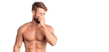 Beyaz bir genç, üstsüz bir şekilde pis ve iğrenç bir koku alıyor. Nefesini burnunda tutuyor. Kötü kokuyor. 