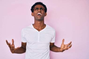 Sıradan giyinmiş, gözlüklü, deli gibi bağıran, sinirli ifadeli ve kollarını kaldırmış Afrikalı yakışıklı bir adam. hüsran kavramı. 