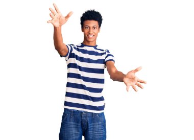 Gündelik giysiler giymiş genç Afro-Amerikan bir adam kameraya sarılıp gülümseyerek bakıyor. Mutluluğu kucaklayan neşeli bir ifade.. 