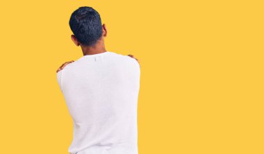 Gündelik kıyafetler giyen genç latin adam kendini kucaklıyor, mutlu ve pozitif. Sevgi ve özgüven. 