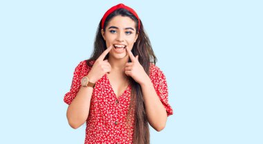 Yazlık elbise giyen esmer kız ağzı açık gülümseyen, parmakları işaret eden ve neşeli gülümsemeye zorlayan. 