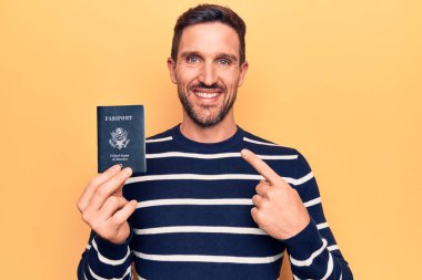 Birleşik Devletler pasaportu taşıyan yakışıklı genç bir turist izole edilmiş sarı arka planda mutlu bir gülümsemeyle el ve parmağıyla işaret ediyor.