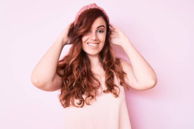 Genç ve güzel bir kadın günlük kıyafetler giyiyor rahatlıyor ve esniyor, kolları ve elleri başının arkasında mutlu bir şekilde gülümsüyor. 