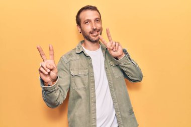 Gündelik kıyafetler giymiş genç yakışıklı adam kameraya bakıp zafer işareti yapıyor. İki numara.. 