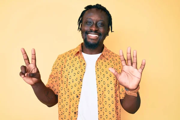 Saçları örgülü genç Afro-Amerikan bir adam 7 numaralı parmaklarını gösterip gösterirken kendinden emin ve mutlu bir şekilde gülümsüyor.. 