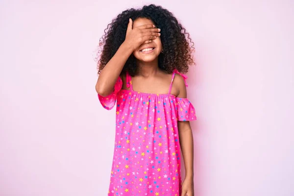 カジュアルなドレスを着た巻き毛のアフリカ系アメリカ人の子供は笑顔で 驚きのために目を覆う顔で笑っています 視覚障害の概念 — ストック写真