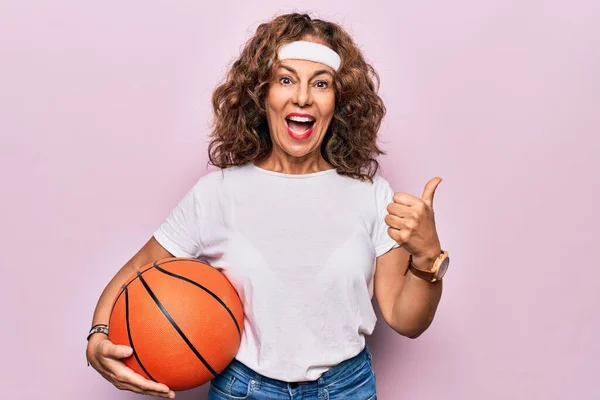中世ブルネットバスケットボールプレーヤー女性保持ゲームボール上の隔離されたピンクの背景Pointing親指へザサイド笑顔満足とともにオープン口 — ストック写真