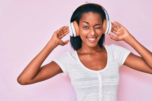 Mujer Afroamericana Joven Escuchando Música Usando Auriculares Guiñando Ojo Mirando — Foto de Stock