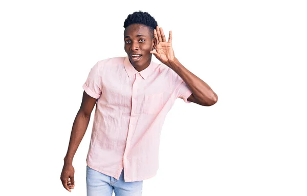 噂やゴシップに耳を傾ける耳に手で笑みを浮かべてカジュアルな服を着て若いアフリカ系アメリカ人の男性 聴覚障害の概念 — ストック写真