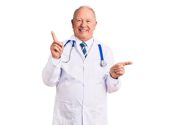 大英俊的白发男人穿着医生的外套和听诊器 自信地微笑着 用手指指向不同的方向 复制广告空间 — 图库照片