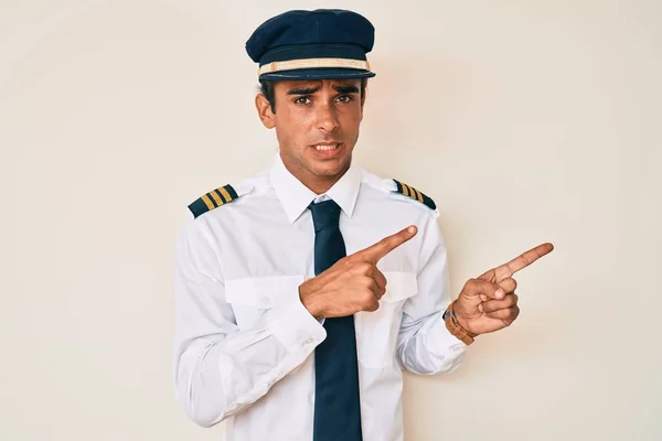 Young Hispanic Man Wearing Airplane Pilot Uniform Pointing Aside Worried — Stock Photo, Image